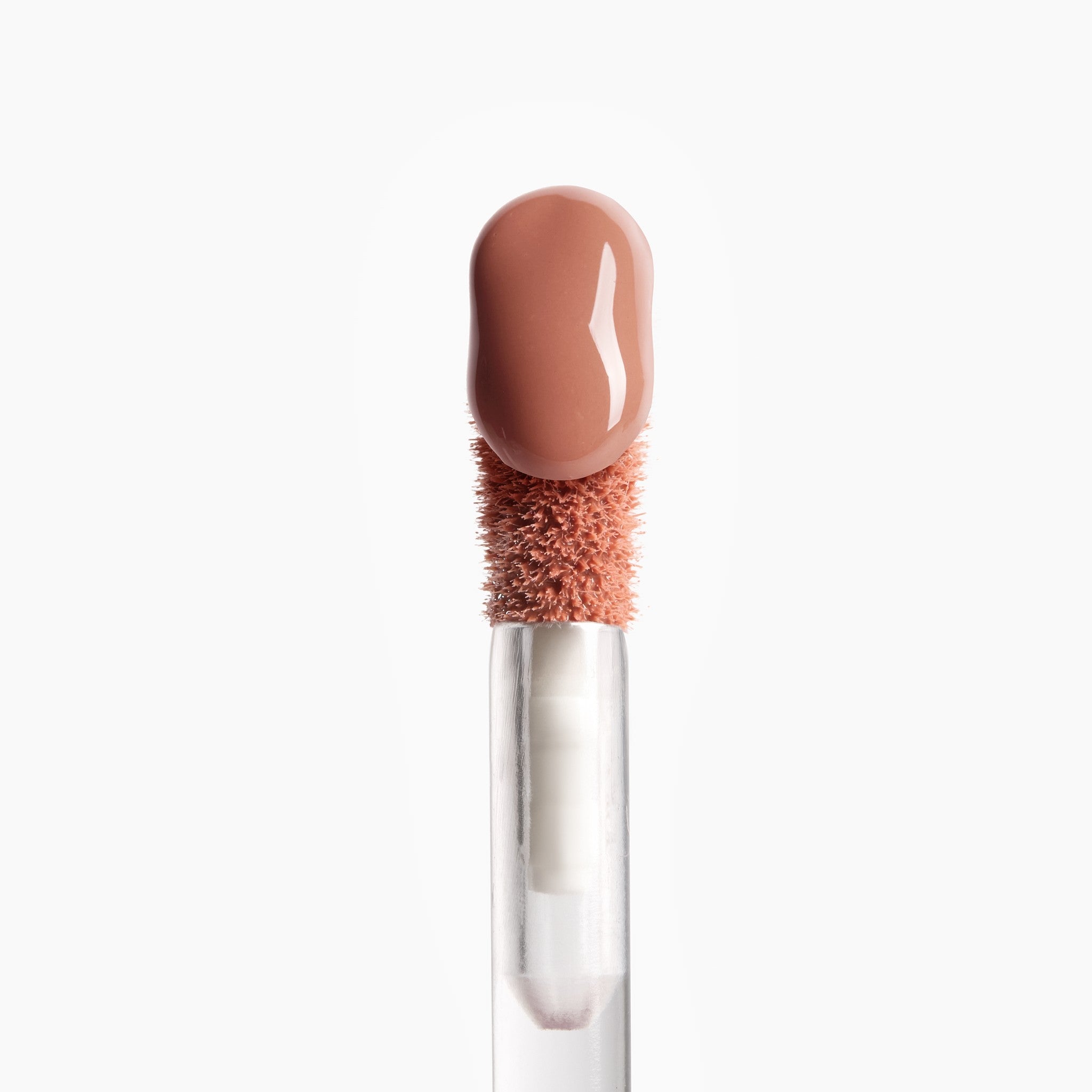 Lip gloss applicator with a nude bristle head and clear handle on a white background