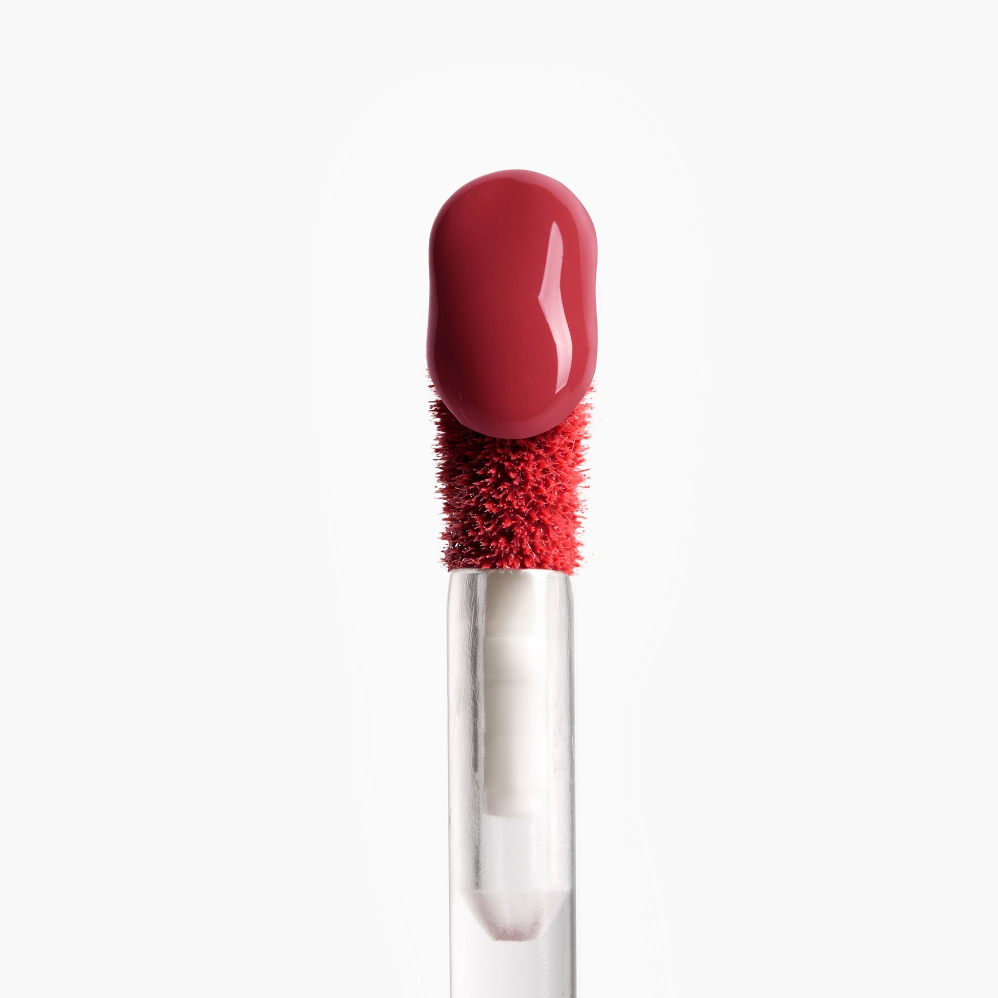 Lip gloss applicator with red bristle head and handle on a white background