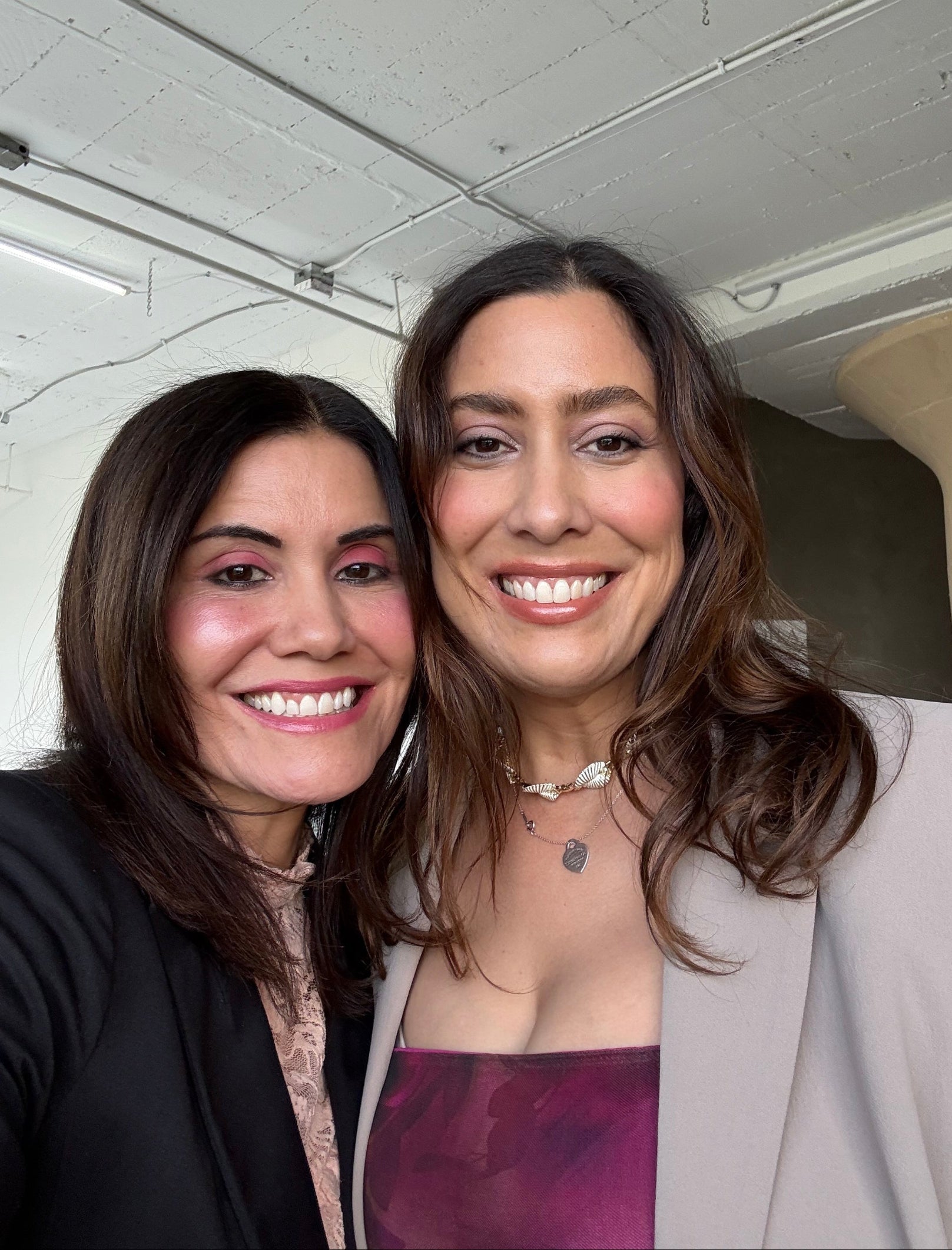 Two women smiling at the camera with a neutral background