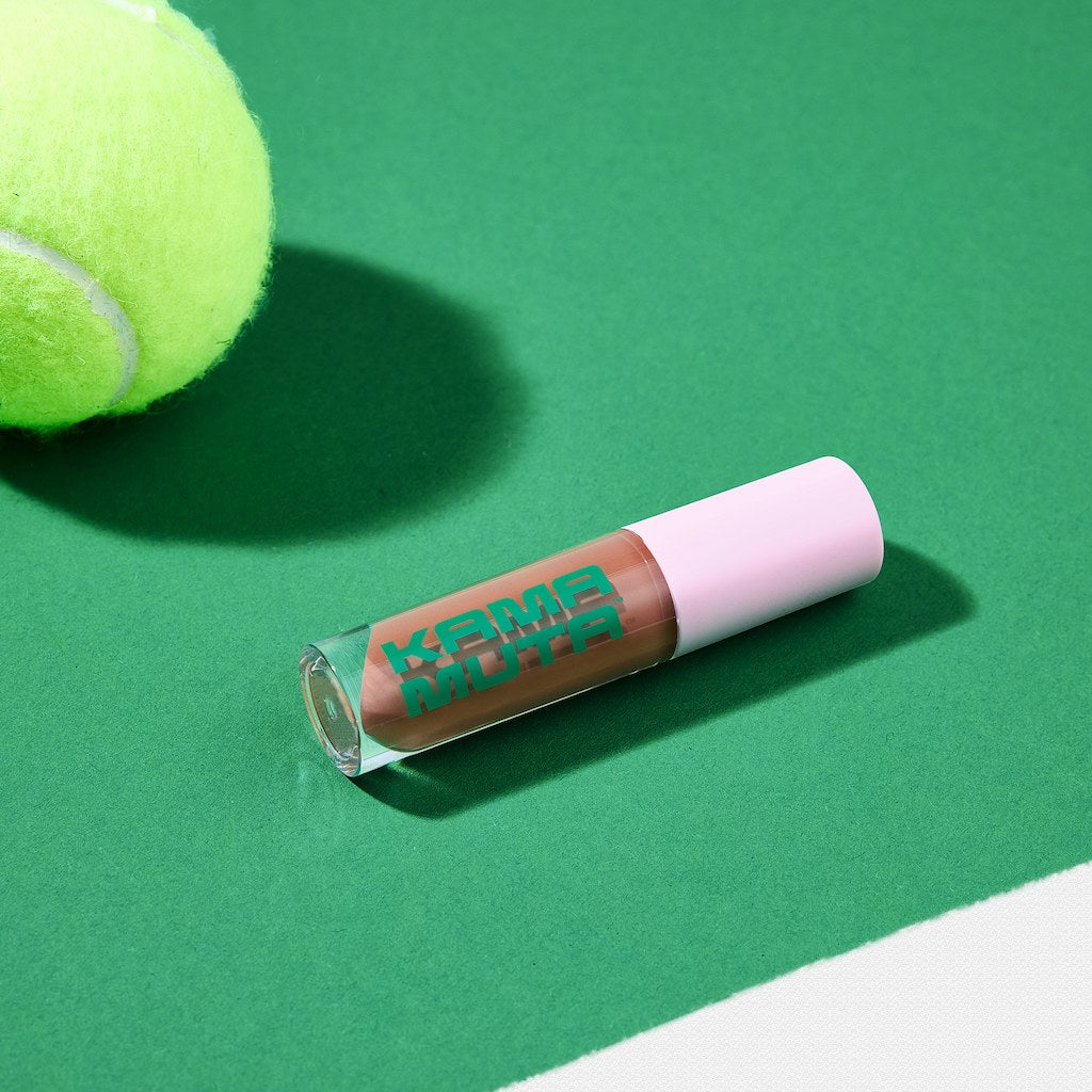 Lip gloss with 'Kama Muta' branding on a green surface next to a tennis ball